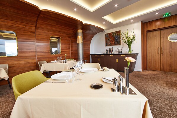 A dining area with a table set for two, a mirror, and a vase with flowers.