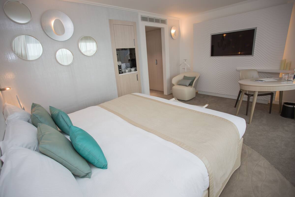 A hotel room with a large bed, a desk, and a chair. There are multiple mirrors on the wall and a television on the wall.