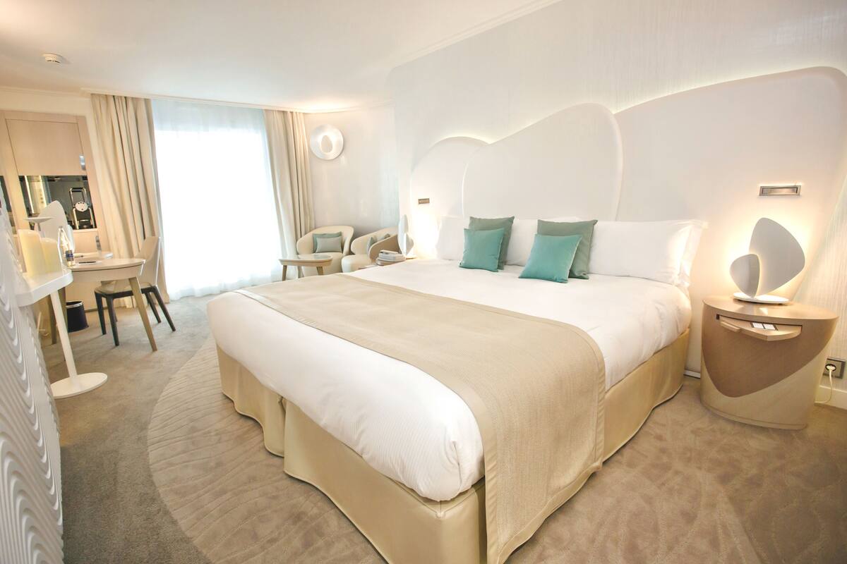 A spacious hotel room with a large bed, a desk, and a chair.
