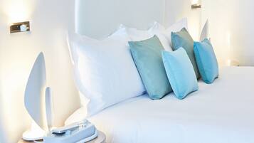 A neatly made bed with white and teal pillows, a bedside table with a lamp, and a wall-mounted light fixture.