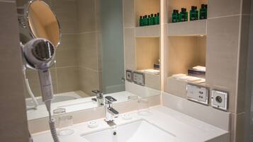 A modern bathroom with a large mirror, a hairdryer, and shelves with toiletries.