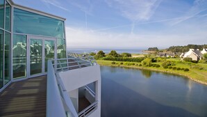 Een modern gebouw met grote glasramen, met uitzicht op een rustig waterlichaam en een verre kustlijn.