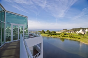 A modern building with large glass windows overlooking a calm body of water and a distant shoreline.
