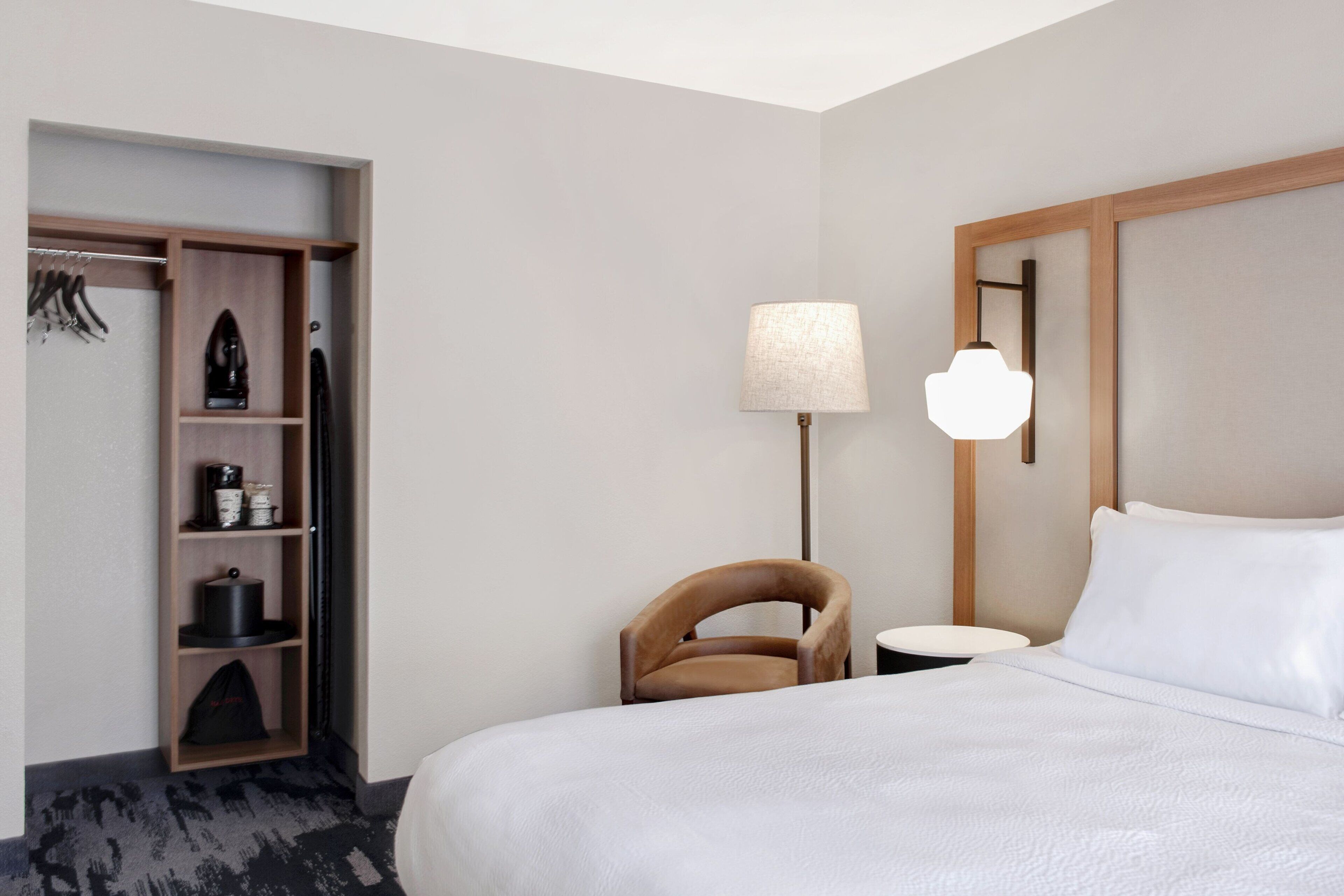 Une chambre d’hôtel comprenant un lit, une chaise, une table de chevet, une lampe et une armoire.