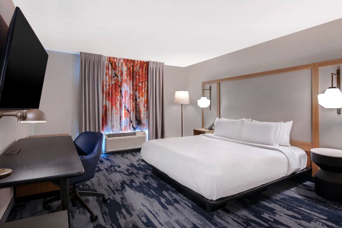 Habitación de hotel con cama, escritorio, silla y televisor.