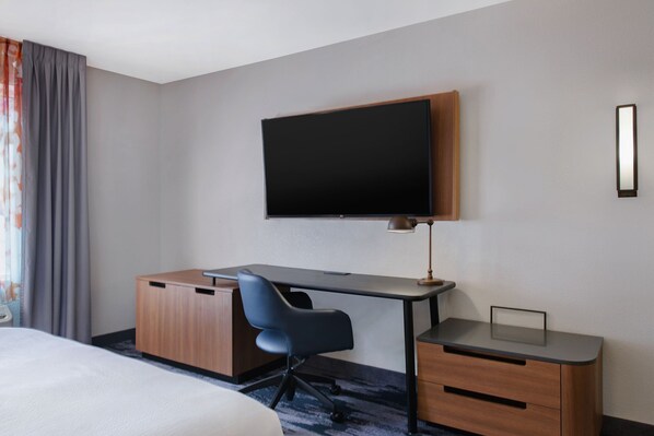 Una habitación de hotel con cama, escritorio, silla, televisor y armario.