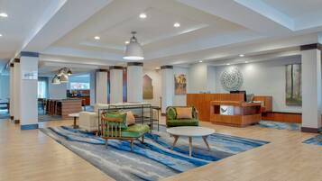 A spacious lobby with a reception desk, seating area with sofas and chairs, and a large window providing natural light.