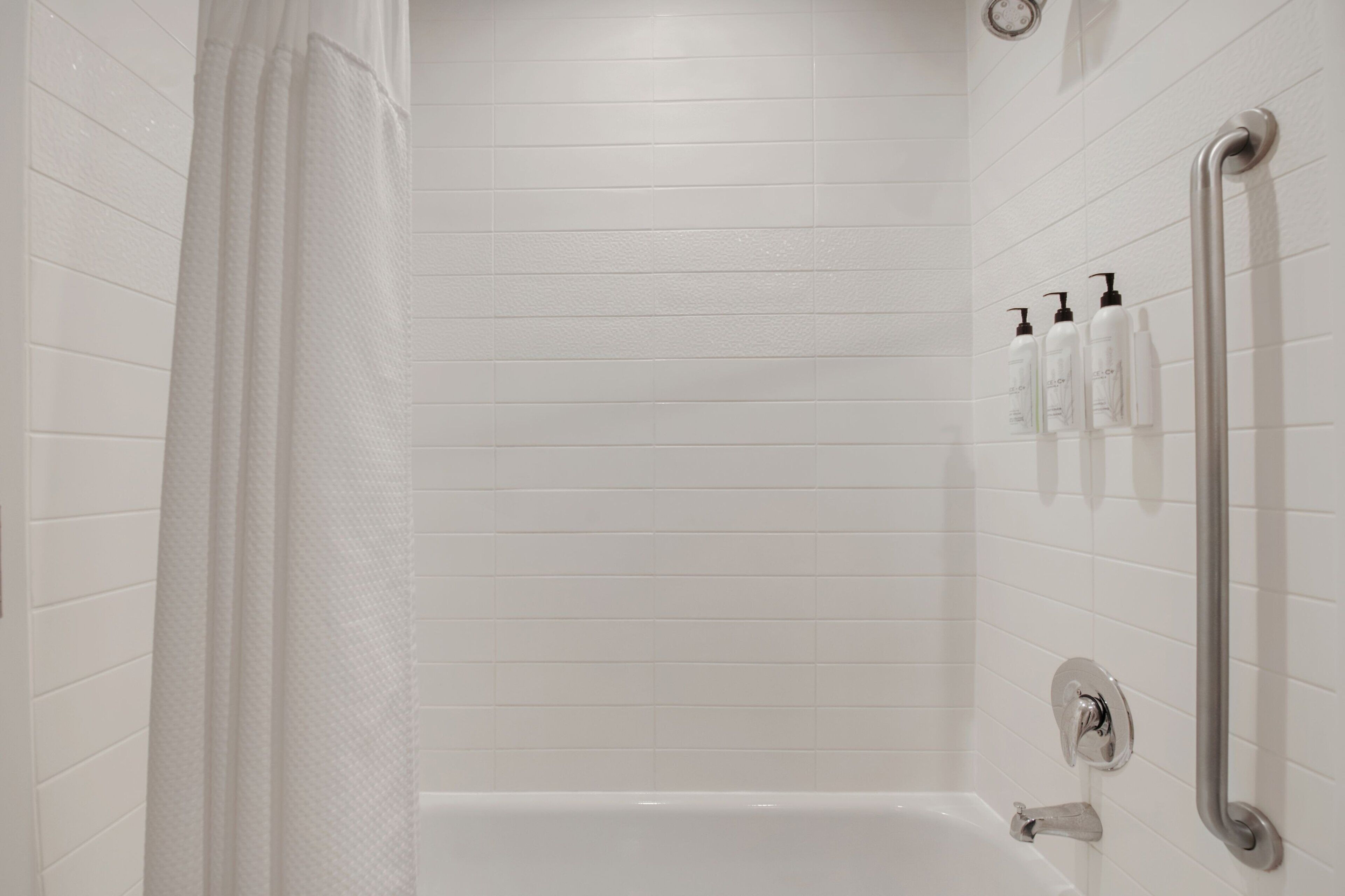 Ein Badezimmer mit weißen Fliesen, einer Badewanne, einer Duschvorhangs und einer Handstange.