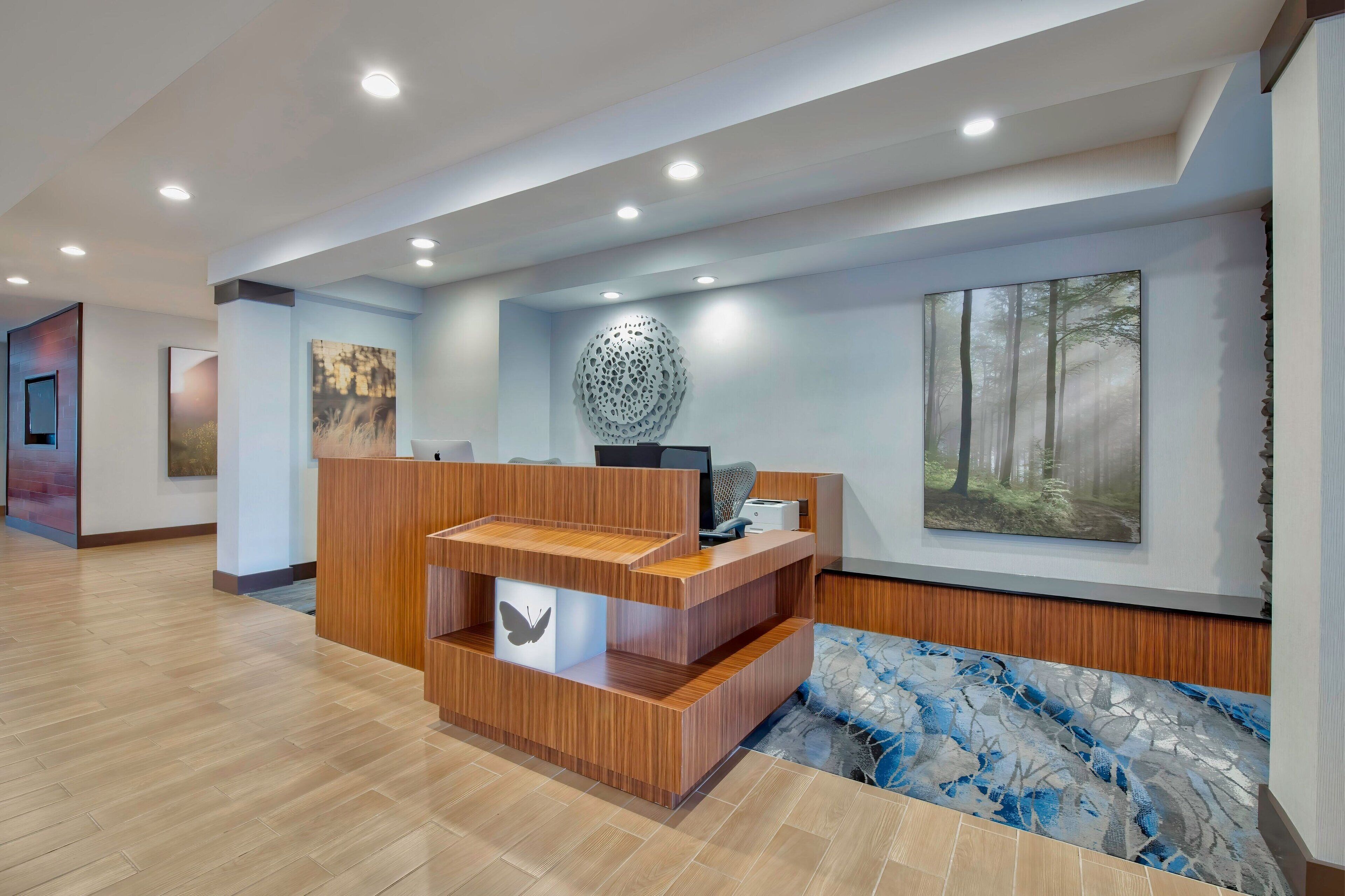 A reception area with a wooden desk, a computer, and a decorative wall piece.