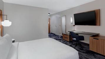 Een hotelkamer met een groot bed, een bureau met stoel, een flatscreen televisie aan de muur en een tafeltje met lamp.