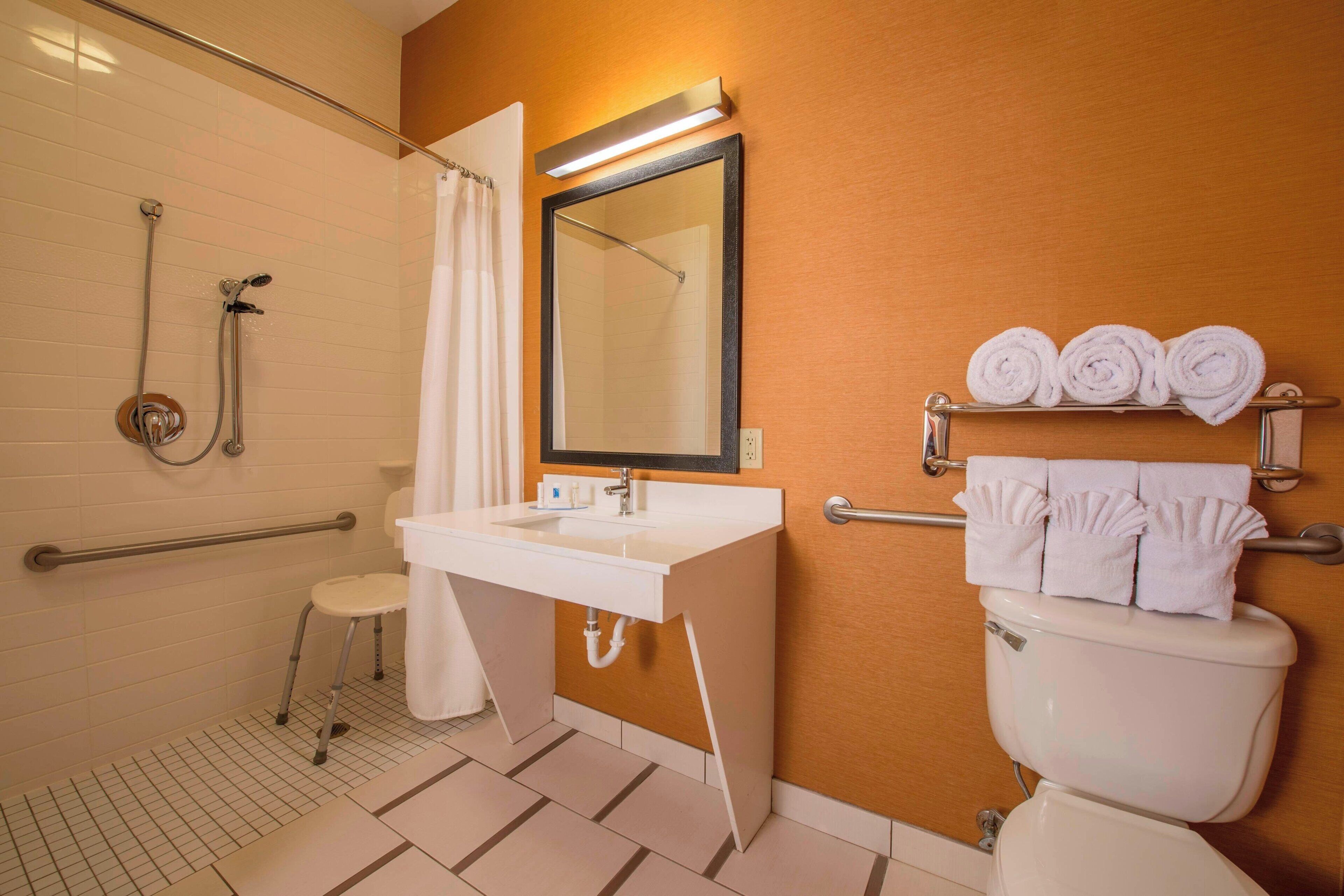 A bathroom with a shower, toilet, sink, and a mirror.