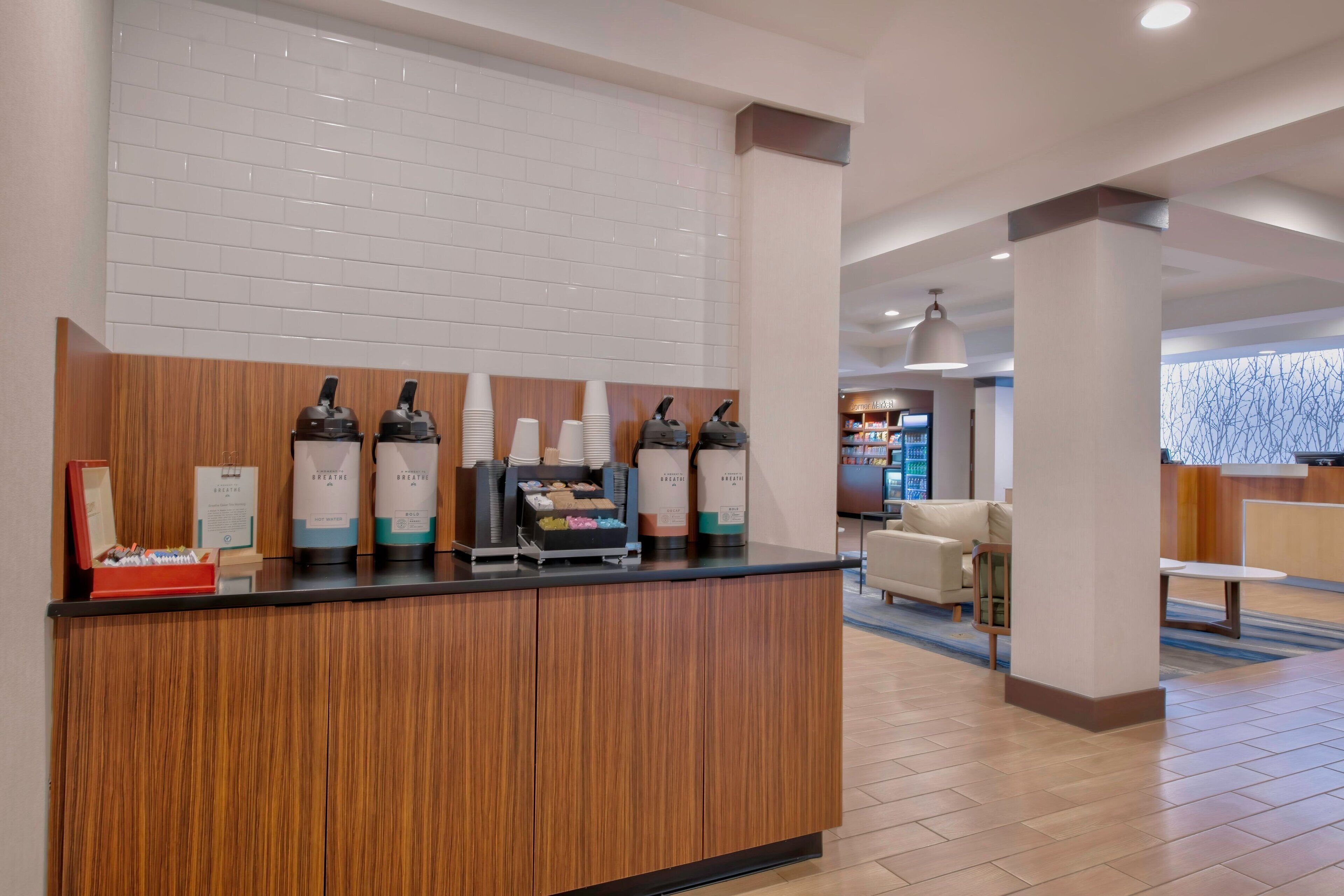 Een receptie met een houten balie, koffieautomaten en een zithoek met een bank en een tafel.