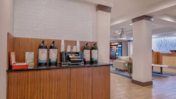Een receptie met een houten balie, koffieautomaten en een zithoek met een bank en een tafel.