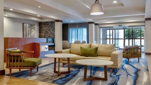 A modern lobby with a beige sofa, two round tables, a wooden chair, a stone accent wall, and large windows.