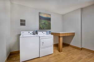 A laundry area with a Whirlpool washer and dryer, a wooden sink, and a painting on the wall.