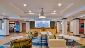 A spacious lobby with a modern design, featuring a seating area with sofas and chairs, a central table, and a large window with a view.