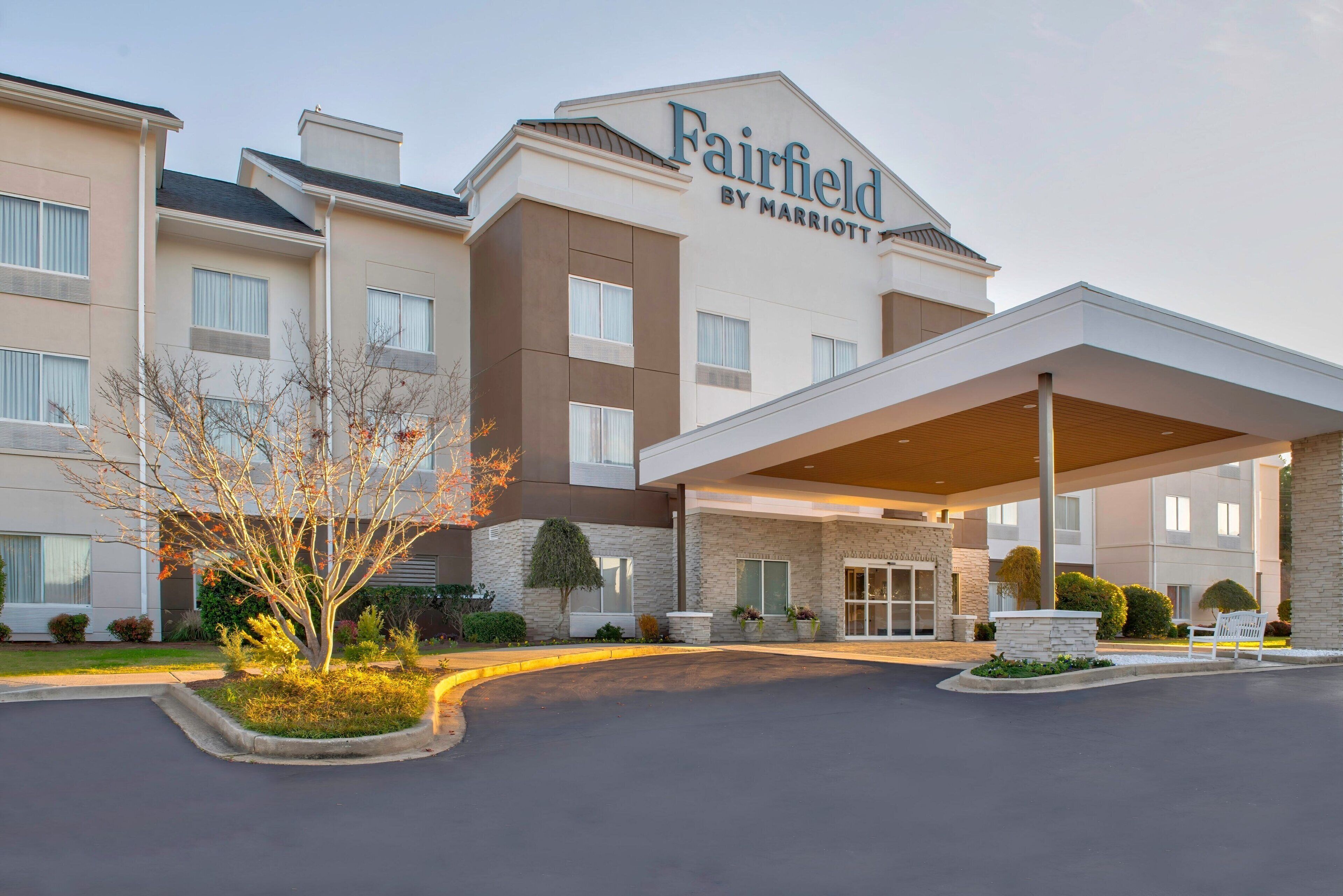 A Fairfield by Marriott hotel with a modern entrance, a covered driveway, and landscaped areas with trees and shrubs.