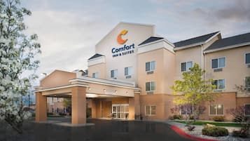 A Comfort Inn & Suites hotel with a modern design, featuring a central entrance, multiple windows, and a landscaped area with trees and shrubs.