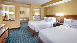 A hotel room with two beds, a desk, a chair, a mirror, and a bathroom visible through an open door.