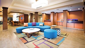 A spacious lobby with a blue sofa, round coffee table, and ottoman, a reception desk, and a dining area in the background.