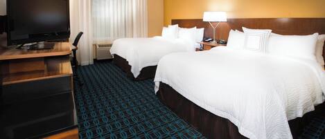 A hotel room with two beds, a desk with a television, and a patterned carpet.