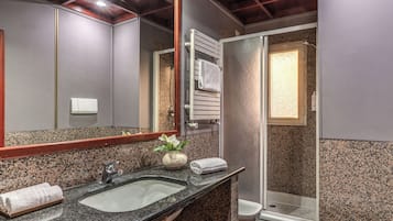 A bathroom with a granite countertop, a sink, a mirror, a towel rack, a shower, and a toilet.