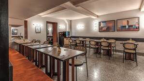 A restaurant with long wooden tables, wicker chairs, and wall-mounted lights.