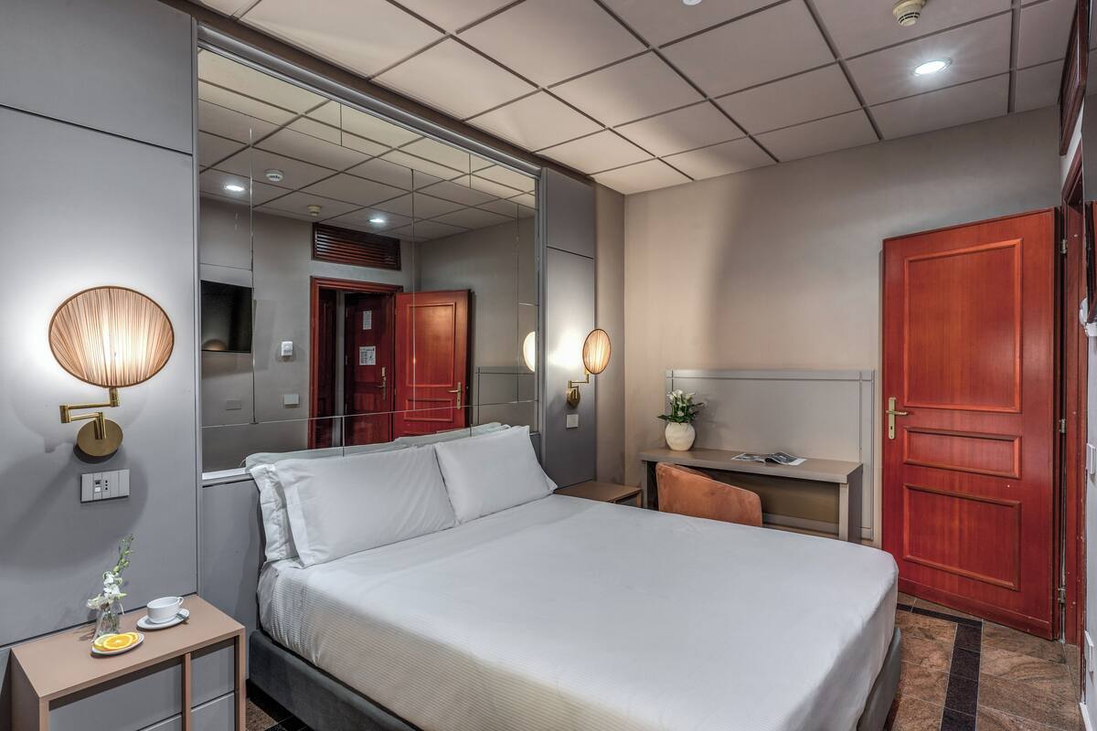 A hotel room with a large bed, bedside tables, a desk, and a wardrobe.