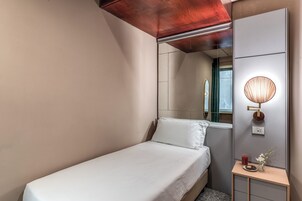 A neatly made bed with white linens, a bedside table with a vase of flowers, and a wall-mounted lamp.