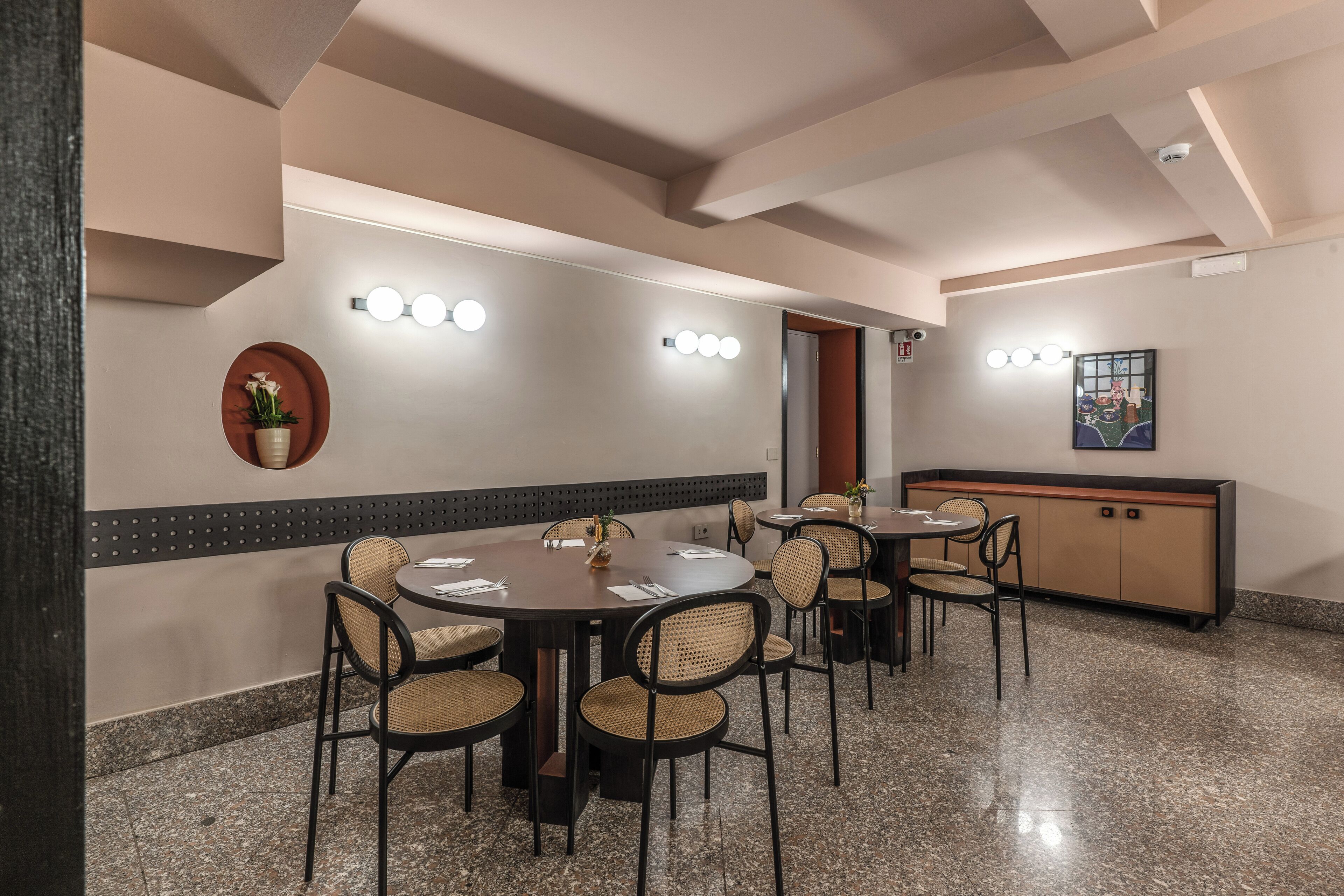 Una sala conferenze con tavoli e sedie rotonde, un lampadario a parete e un mobile contenente un oggetto decorativo.