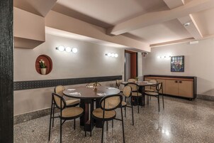 A conference room with round tables and chairs, a wall-mounted light fixture, and a cabinet with a decorative item.