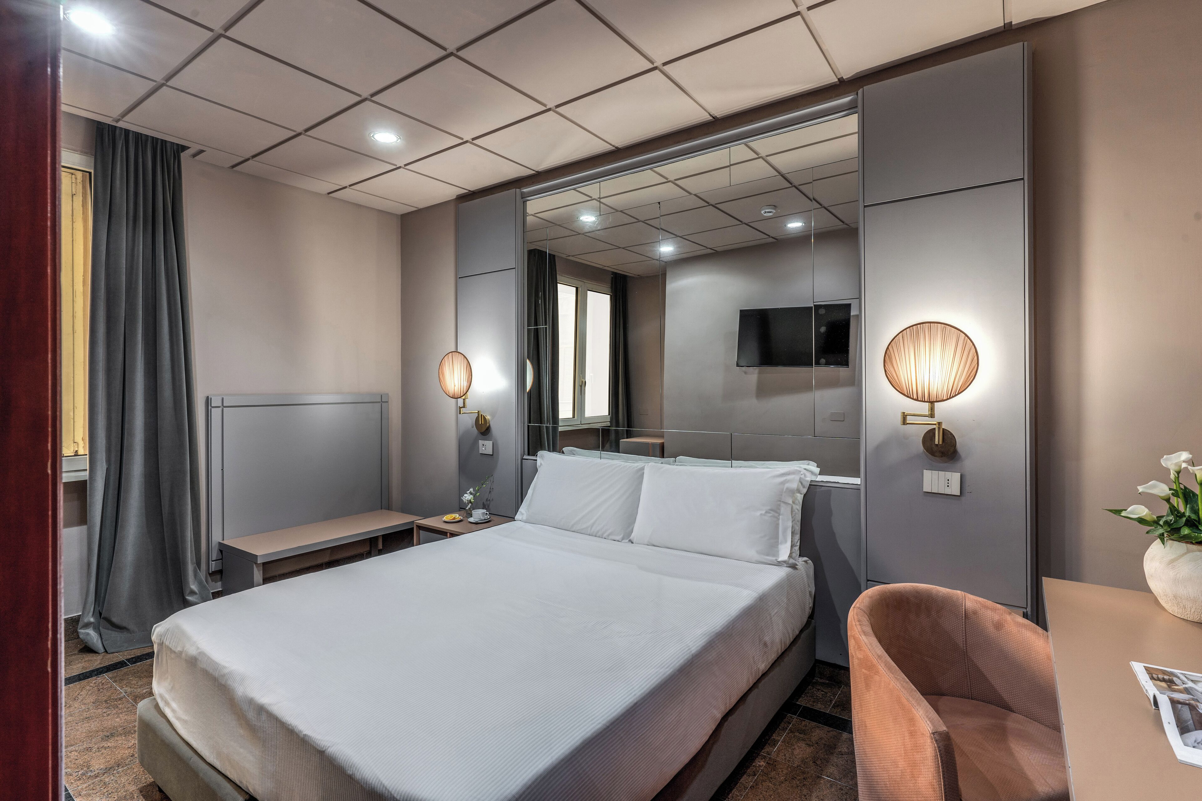 Quarto de hotel moderno com uma cama grande, mesas de cabeceira, uma TV e um espaço de estar.
