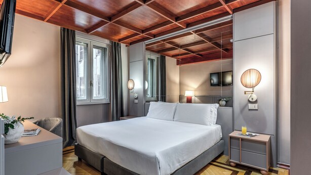 A modern bedroom with a large bed, bedside lamps, a flat-screen TV, and a wooden ceiling.