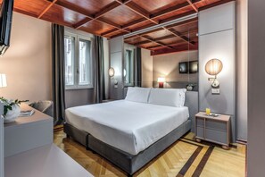 A modern bedroom with a large bed, bedside lamps, a flat-screen TV, and a wooden ceiling. - Hotel Madison (Rome)
