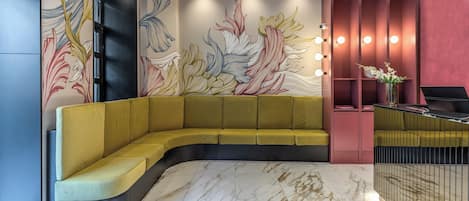Un espace d’accueil moderne avec un canapé jaune aux lignes courbes, un sol en marbre et un mur orné d’œuvres d’art florales abstraites.