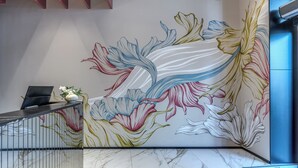 A reception area with a marble floor, a reception desk, a laptop, and a floral mural on the wall.