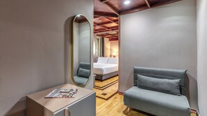 A modern hotel room with a wooden ceiling, a grey sofa, a small table with a magazine, and a large mirror.