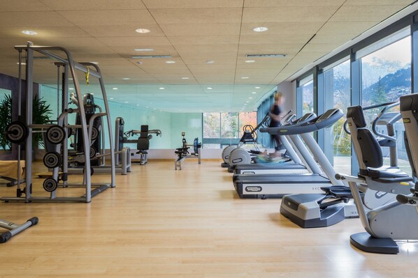A gym with cardio machines, weightlifting equipment, and large windows offering a view of mountains. - Andorra Park Hotel (Andorra la Vella)