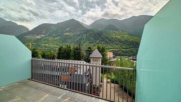 Un balcon doté d’une balustrade en métal, qui offre une vue sur un paysage montagneux, avec une petite tour et un espace de stationnement.