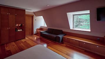 Un dormitorio moderno con suelo de madera, cama, sofá, armario y ventana con vistas a zonas verdes.