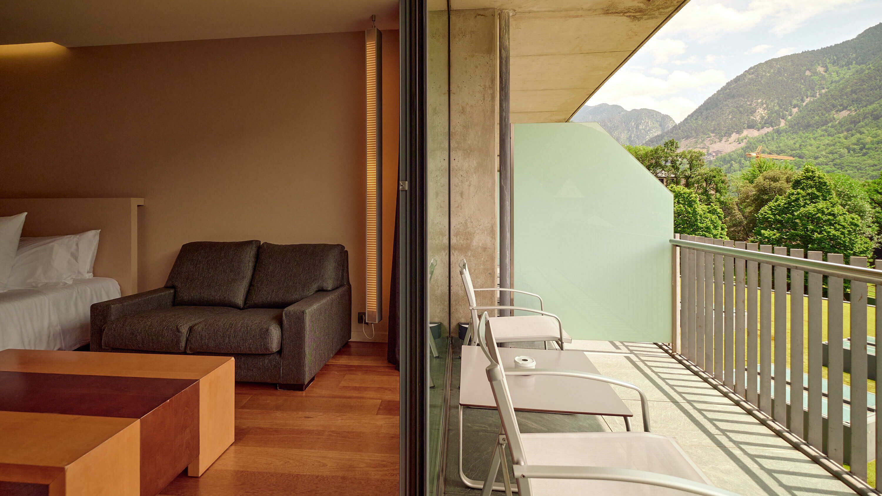 A modern hotel room with a balcony, a sofa, a bed, and a table.