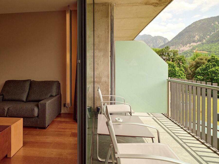 A modern hotel room with a balcony, a sofa, a bed, and a table.