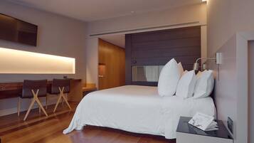 Een moderne hotelkamer met een groot bed, een bureau met stoelen en een flatscreen televisie aan de wand.