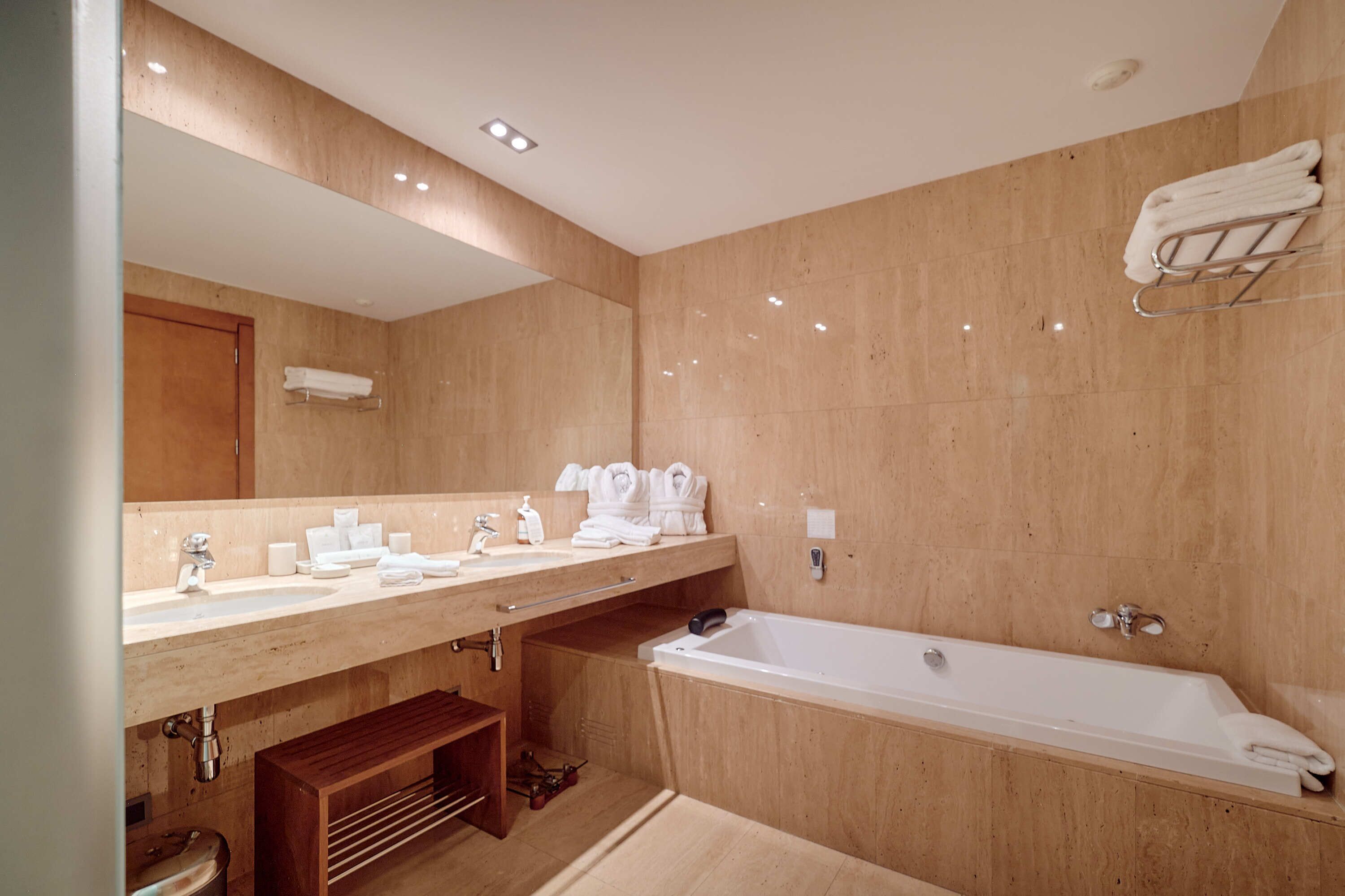 Un baño moderno con un espejo grande, lavamanos dobles, bañera y tocador de madera.