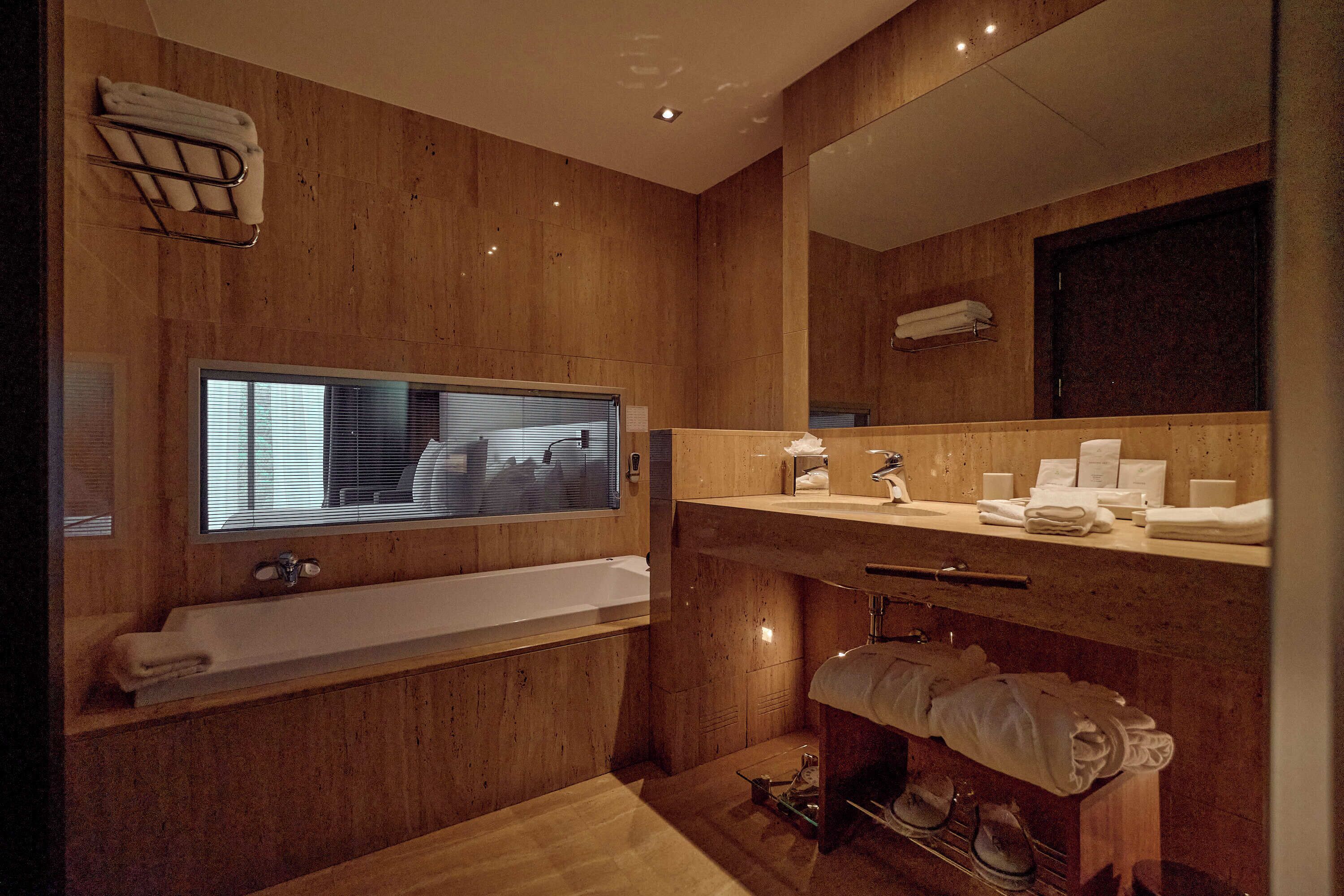 A modern bathroom with a wooden finish, a large window, a bathtub, a vanity with a mirror, and a towel rack.