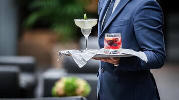 A person in a blue suit holding a tray with a martini glass and a glass of red drink.