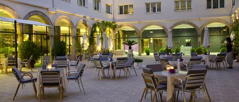 A courtyard with outdoor seating, arches, and a building facade.