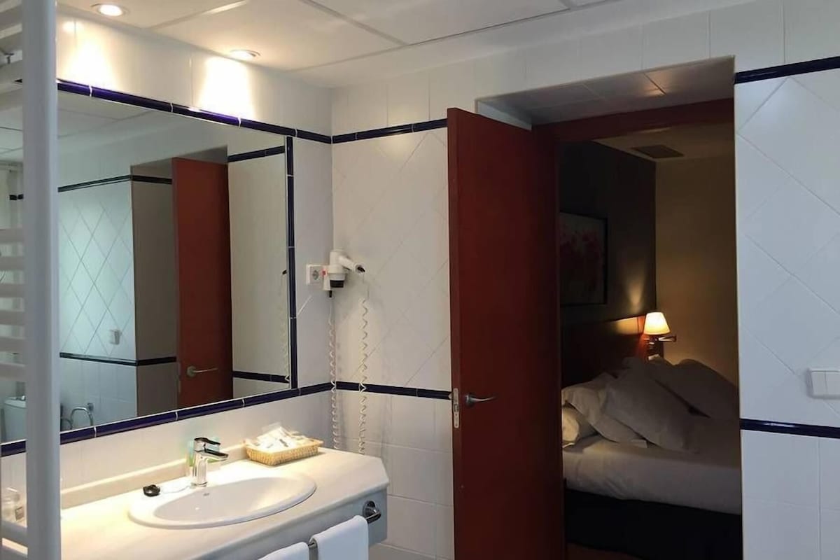 A hotel bathroom with a sink, mirror, and a door leading to a bedroom.