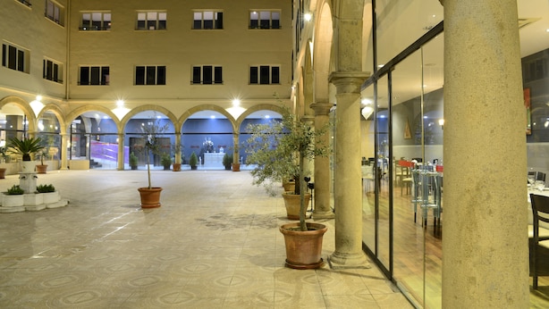 Un amplio patio con numerosas plantas en macetas, una fuente central y una zona de estar con mesas y sillas.