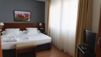 Una habitación de hotel con una cama grande, una mesita de noche con lámpara, un televisor y un cuadro en la pared.